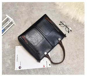 Detailed view of black tote bag with brown handles and decorative zippers on stone floor