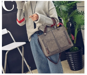 Detailed view of grey tote bag with dual front zippers and brown leather handles
