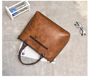 Top view of a brown vintage oil leather tote bag on a marble floor with lifestyle props