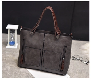 Detail view of a gray PU leather tote bag featuring brown handles and large front zippers