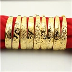 Detailed view of nine gold-plated bangles with intricate engravings on red velvet display