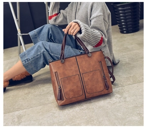 Detail of a brown PU leather tote bag with zip pockets shown in a lifestyle street setting