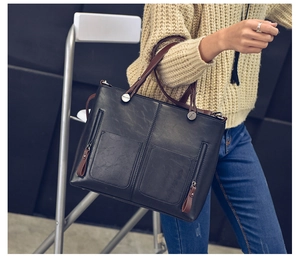 Fashionable black tote bag with brown straps styled on a model with beige knitwear