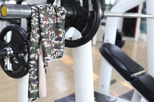 Macro shot of camouflage cooling sports towel hanging on barbell in gym setting