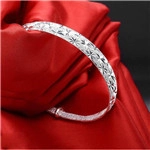 Macro shot of silver hollow-out flower engraved bracelet on elegant red silk fabric