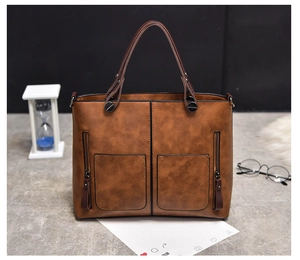 Detail of a brown leather tote bag featuring two front zipper pockets and top handles