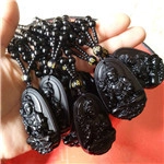 Close-up of hand holding multiple black obsidian Buddha pendants with gold bead necklaces