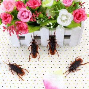 Realistic brown cockroach prank toys shown with decorative white fence and flowers