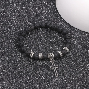 Detail of black lava stone yoga bracelet with silver cross pendant on sparkly surface