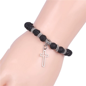 Detailed view of matte black volcanic stone yoga bracelet with silver cross charm on wrist