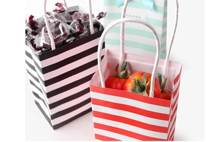Detailed view of striped paper gift bags in red, black and blue with white rope handles