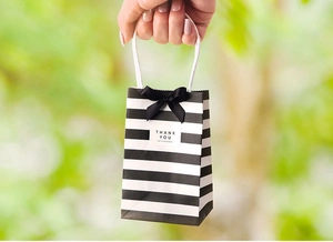 Close-up of small black and white striped paper gift bag with bow and Thank You tag