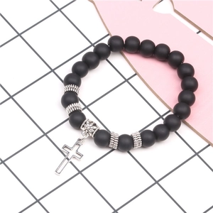Detail of matte black onyx yoga bracelet with silver cross pendant on a white grid mat