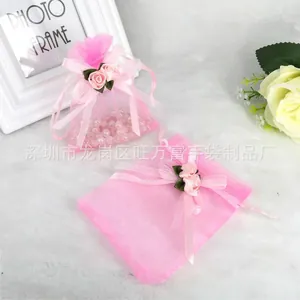 Pink organza drawstring gift bag with satin ribbon bow and rose on white plush background