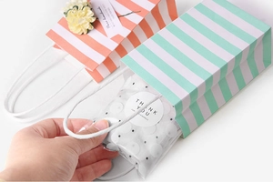 Detail of hand removing thank you gift from striped paper bag with floral accent