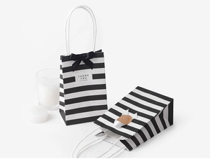 Detail of white kraft paper gift bags with black stripes and elegant bow ribbons