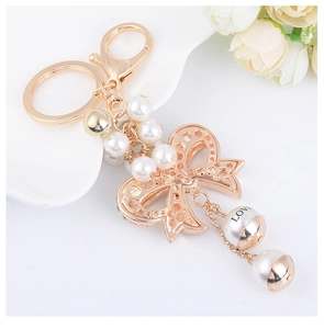 Detail of rose gold bow keychain with white pearls and LOVE charm on white plate