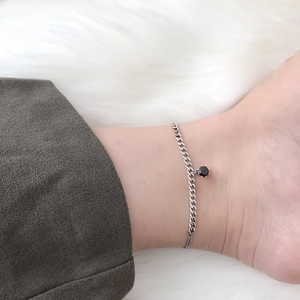 Detailed view of silver chain anklet with black zircon pendant worn on the ankle