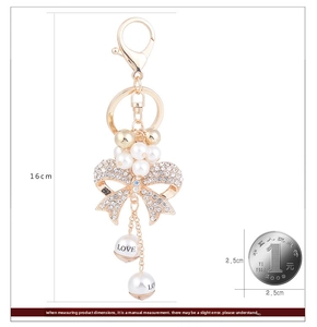Detail of bowknot keychain with crystals, pearls and size reference with a coin