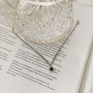 Detail of silver Cuban chain anklet with a black circular gemstone on a vintage book