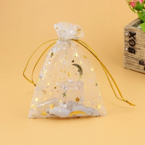 Detailed view of white organza gift bag with gold stars and moons on orange background