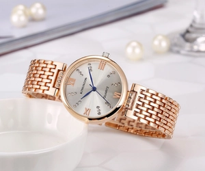 Close-up of rose gold stainless steel watch with crystal markers on a white ceramic bowl