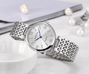 Detail of silver ladies quartz watch with blue hands and crystal markers on white ceramic