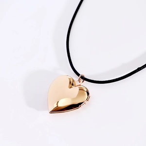 Close-up of heart-shaped gold locket pendant with a black cord necklace on white backdrop