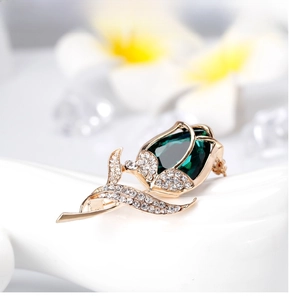 Macro shot of rose brooch featuring emerald pear-cut stone and pavé crystal leaves