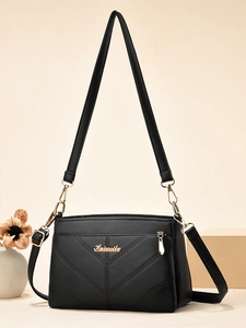 Détail du cuir noir grainé avec coutures en V et logo métallique doré sur le sac à main