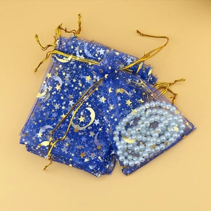 Close-up of blue organza gift bags with gold star moon patterns and pearl jewelry