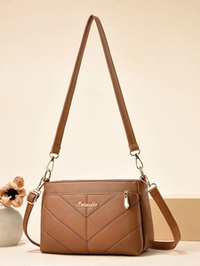 Détail de la texture cuir grainé marron et des coutures en V sur le sac à bandoulière