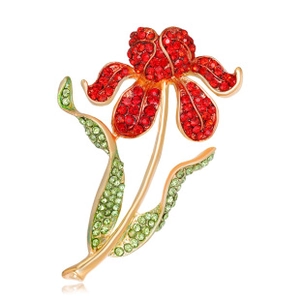 Macro shot of a golden floral brooch with red crystals and green rhinestone leaves