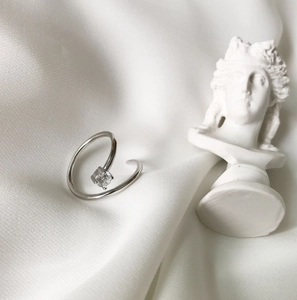 Macro shot of silver spiral ring with square zircon on soft white silk fabric