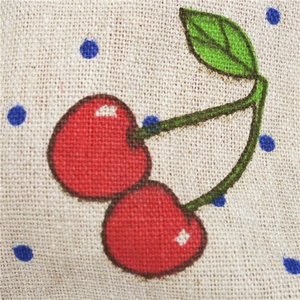 Close-up of beige linen fabric with printed red cherry patterns and blue dots detail