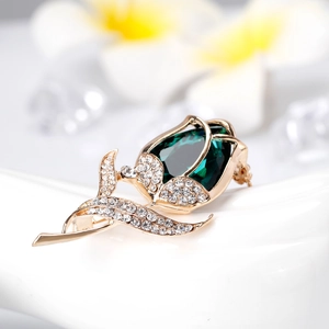 Elegant rose brooch in gold metal with a large emerald green gemstone and white crystals
