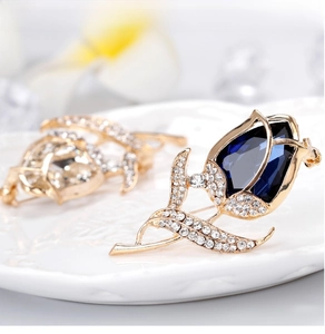 Detailed view of rose flower brooch with blue teardrop gemstone and crystals on gold base