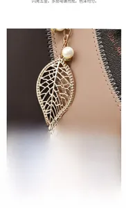 Detailed view of bicolor leather handbag featuring gold leaf pendant and white pearl charm