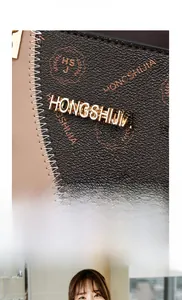 Detail of the cross-grain leather texture and the golden metal HONGSHIJIA logo on the handbag