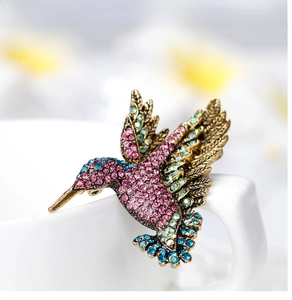 Macro detail of a colorful rhinestone hummingbird brooch on a vintage gold metal base