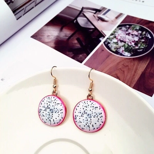 Detailed view of dragon fruit slice earrings with gold hooks on a white ceramic plate
