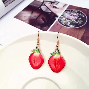 Macro detail of red strawberry earrings with green leaves on white ceramic plate