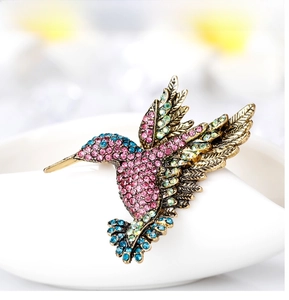 Macro shot of hummingbird brooch with pink and blue rhinestones on white ceramic edge