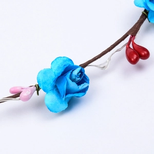 Detailansicht blauer Rosen und roter Beeren an einem leuchtenden Blumenkranz