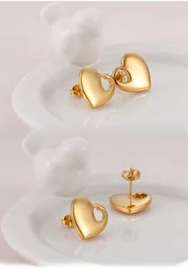 Macro detail of 18K gold plated heart stud earrings with hollow design on white tray