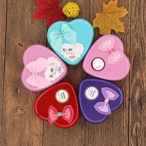 Macro top view of colorful heart-shaped tin gift boxes with bows on dark wood background