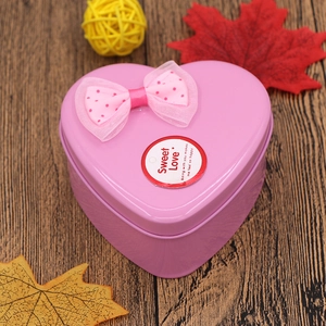 Pink heart-shaped metal tin box with bow and Sweet Love text on wooden background