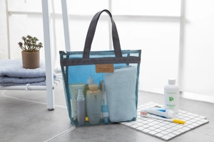 Dettaglio del beauty case in rete blu con toppa in pelle su piastrelle del bagno