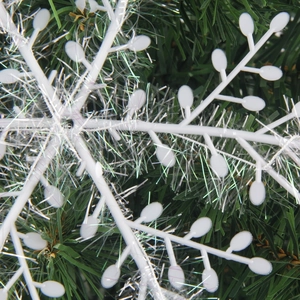 Close-up of white snowflake ornament with silver tinsel on green Christmas tree branches