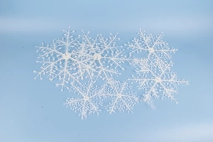 Detail of white glittery snowflake ornaments on light blue background, holiday decorations